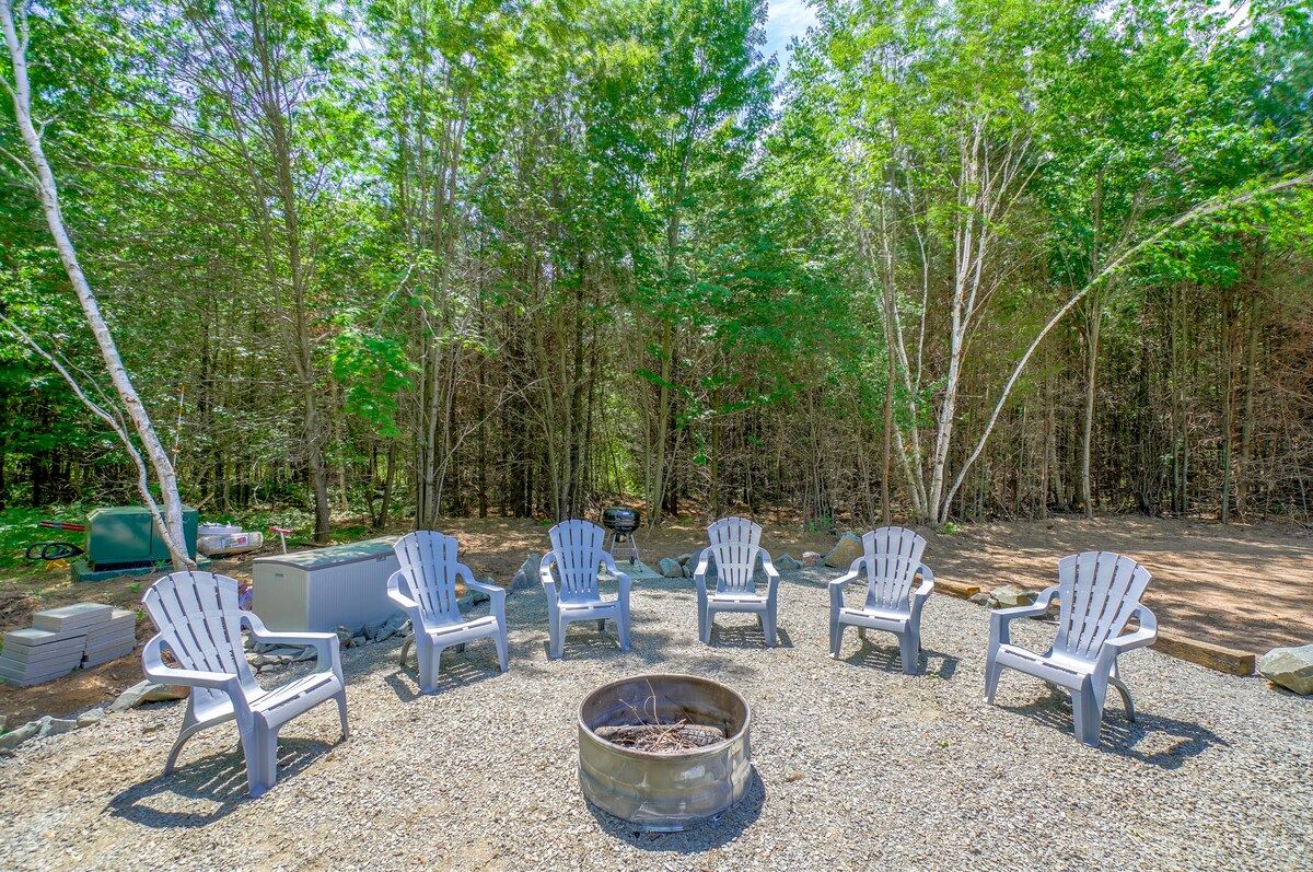 Firepit circled by Adirondack chairs in the summer woods at Cornerstone Cabin